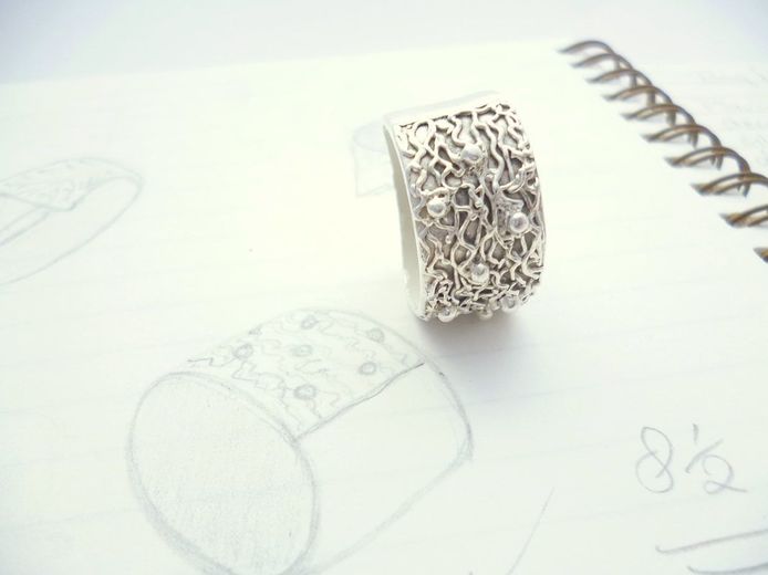 Custom work image of chunky lacey silver ring resting on sketch book
